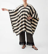 Woman wearing a black and white striped poncho and pants with fringe details on a white background