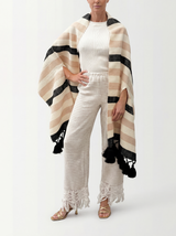 Woman wearing a white outfit with a striped beige and black shawl on a white background
