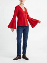 Person wearing a red blouse with flutter sleeves and blue jeans on a white background