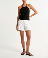Woman wearing a black halter top and white shorts on a white background