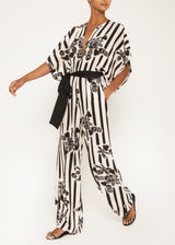 The model is wearing a black and white floral jumpsuit with floral prints and a black belt