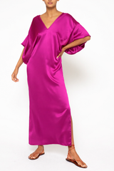 A woman wearing a fuschia pink silk maxi dress with 3/4 sleeves and V neck and side slits 