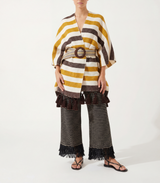 Person wearing a striped poncho with tassels  and pants with fringes on a white background