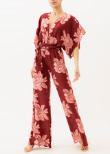 Model wears a red and pink floral jumpsuit with belt