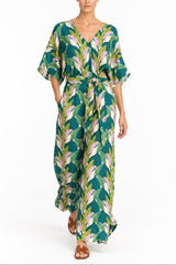 A woman modeling a green and white tropical leaf print kaftan dress with a tie waist, shown against a plain white background.