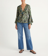 Woman wearing a green leopard patterned blouse with flutter sleeves and blue jeans on a white background