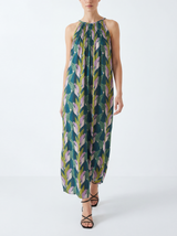 Woman wearing a sleeveless, long, green tropical leaf print dress on a white background
