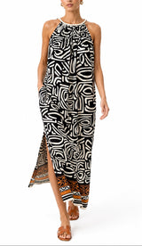 A woman modeling a sleeveless halter-neck maxi dress with a bold black and white abstract pattern and a brown patterned hem, set against a plain white background.
