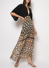 The model is wearing a black dress with a beehive patterned finish, a plunging neckline, an open back, and an A-line maxi cut. 