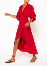 The model is wearing a red maxi dress showcasing an empire-waistline, a deep V-neck, halved kimono sleeves, a concealed hook eye closure, and a wrap skirt.