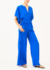 The model is wearing a cobalt blue jumpsuit and matching belt