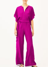 The model is wearing a pink long jumpsuit with a  belt