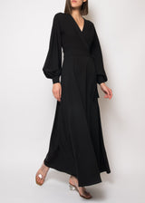The model is wearing a Long sleeve black silk maxi dress featuring long sleeves, a surplice neckline, a backless cut, lantern sleeves with button cuffs, and a wrap front.