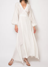 The model is wearing a white dress featuring long sleeves, a surplice neckline, a backless cut, lantern sleeves with button cuffs, and a wrap front.